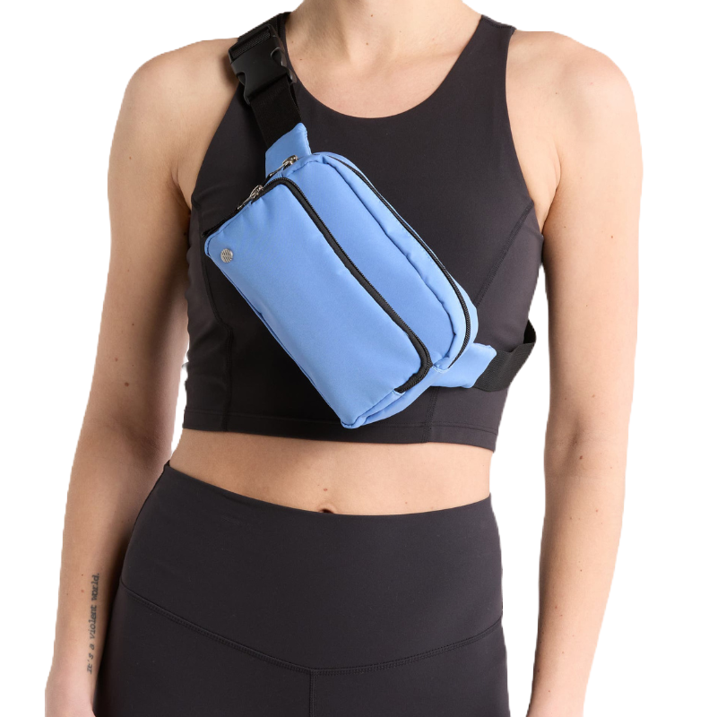 A light blue belt bag with two zippered compartments, featuring black straps and buckle closure, worn across the chest over a black sports bra.