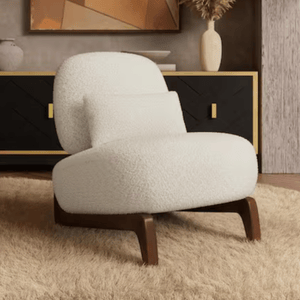 A white, cushioned armchair with wooden legs sits on a beige rug in front of a black and gold sideboard adorned with vases and abstract wall art.