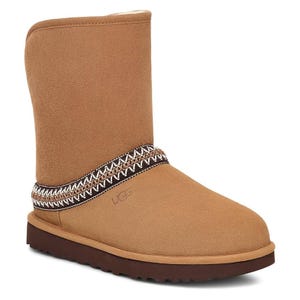 UGG Classic Short Sheepskin Boots in brown feature a suede exterior with a decorative woven band around the ankle and a soft, plush lining. The boots have a flat, cushioned sole for comfort and a rounded toe design.