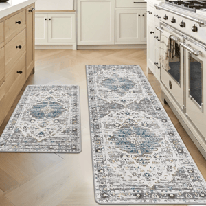 Two kitchen rugs with intricate blue and gray patterns are placed on a light wood floor between white cabinetry and a stove.
