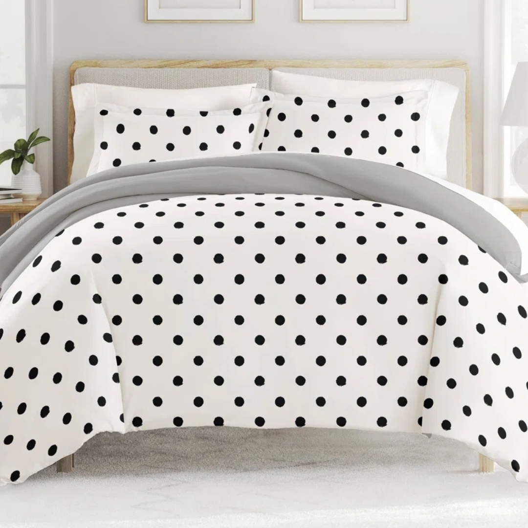 A bed is covered with a white duvet set featuring a black polka dot pattern, complemented by matching pillowcases and a light gray blanket.