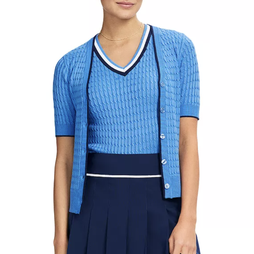 A model wears a light blue knit cardigan and V-neck top with a navy pleated skirt and cap, styled for a casual or sporty look.