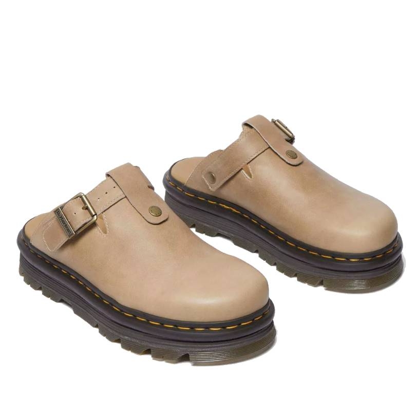 Beige leather mules with a closed round toe, chunky sole, and adjustable strap with a metal buckle. Features a thick sole with signature yellow stitching.