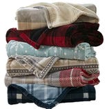 A stack of six folded blankets featuring various patterns, including plaid, snowflakes, and geometric designs, in colors like beige, red, blue, and grey.