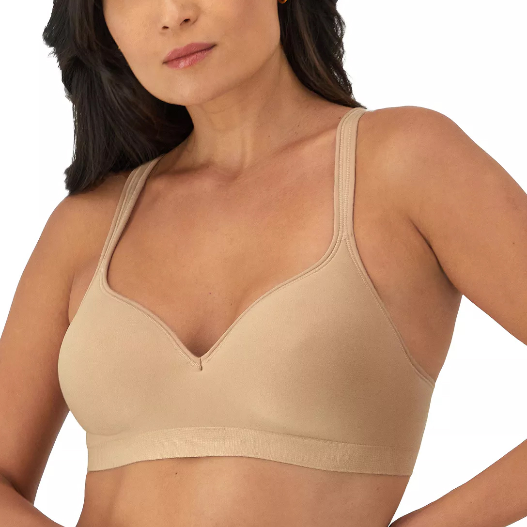 A woman is wearing a beige, wireless bra with wide straps and seamless cups, providing a smooth look and support.