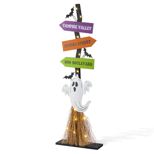A Halloween-themed sign with three arrowed directions labeled \“Vampire Valley,\“ \“Spooky Street,\“ and \“Boo Boulevard,\“ adorned with a ghost, bats, and lit with string lights at the base.
