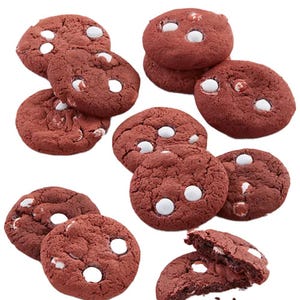 A dozen red velvet cookies with visible white chocolate chips scattered on top and throughout. One cookie is broken, showing the soft texture inside.