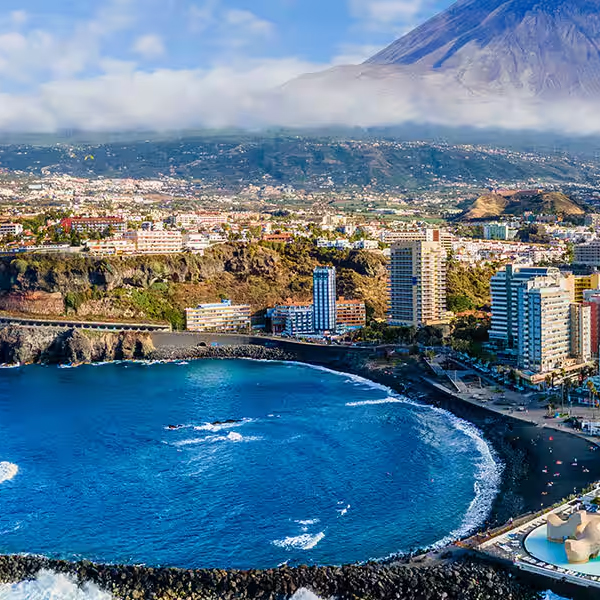 A coastal cityscape with ocean waves, high-rise buildings, and a prominent mountainous backdrop.