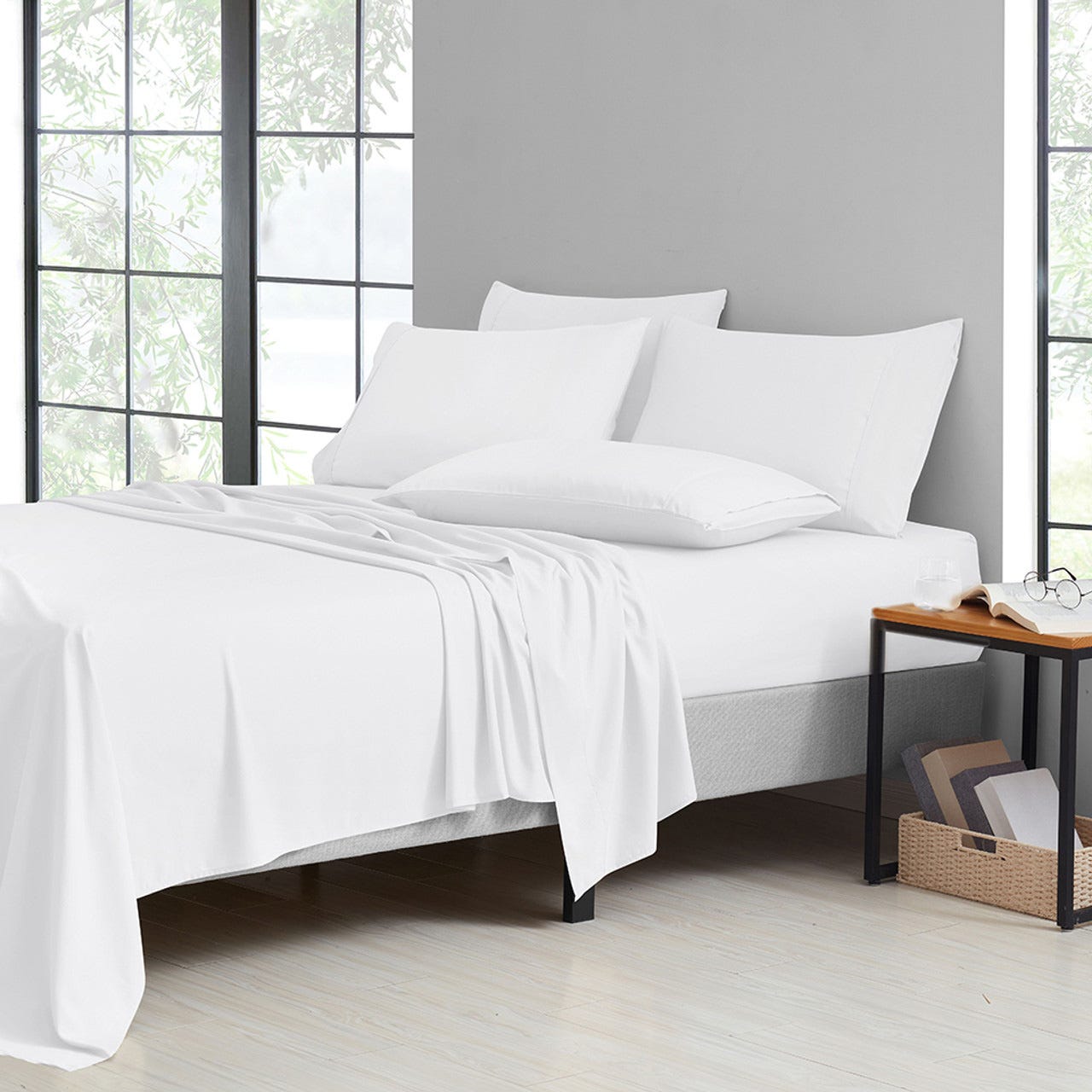 A neatly made bed with white sheets, pillowcases, and a light blanket, next to a bedside table with a glass and eyeglasses.