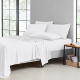 A neatly made bed with white sheets, pillowcases, and a light blanket, next to a bedside table with a glass and eyeglasses.