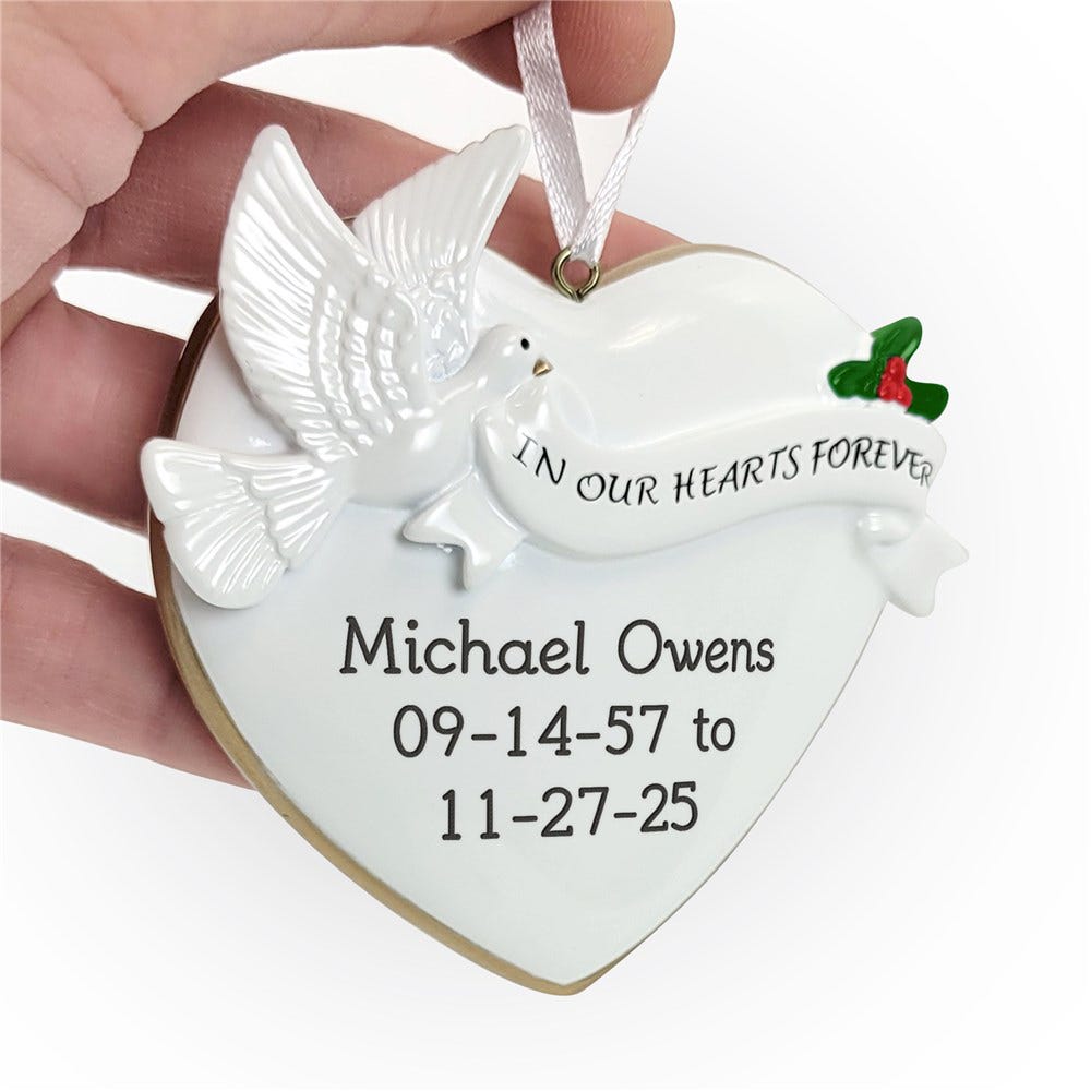 A heart-shaped memorial ornament featuring a white dove, with the inscription \“IN OUR HEARTS FOREVER.\“ Engraved below are the name Michael Owens and dates 09-14-57 to 11-27-25.