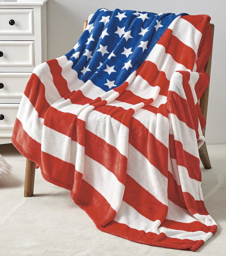 A fleece blanket featuring an American flag design with red and white stripes and a blue field with white stars draped over a chair.