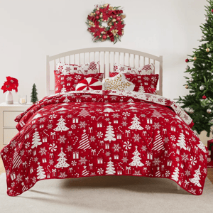 A festive bedding set with a red Christmas-themed pattern featuring trees, presents, and snowflakes. The room is decorated with a wreath, a Christmas tree, and poinsettias, creating a holiday ambiance.