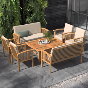 Outdoor patio set with wooden slatted table, two cushioned sofas, and four cushioned armchairs. Surrounded by greenery on a tiled surface.