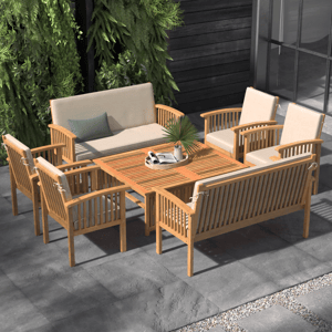 Outdoor patio set with wooden slatted table, two cushioned sofas, and four cushioned armchairs. Surrounded by greenery on a tiled surface.
