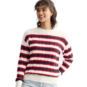 A person wears a striped sweater with red, white, and blue horizontal lines and light-colored jeans.