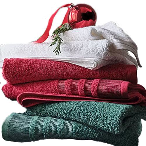 A stack of folded towels in shades of green, red, and white with a decorative red ornament and evergreen sprig placed on top.
