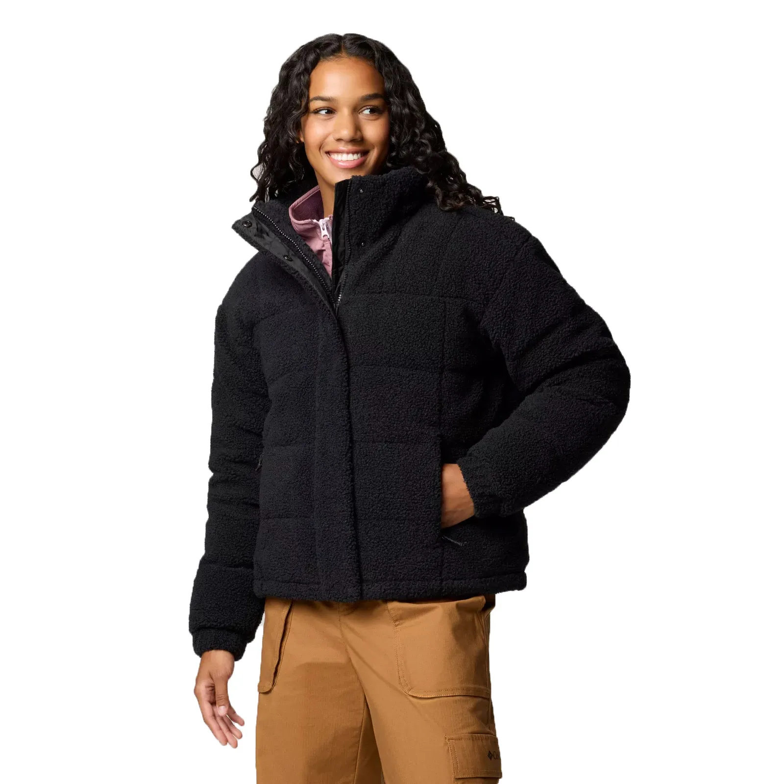 The Columbia Ruby Falls Down Jacket is a black, insulated, and quilted jacket designed for warmth. It features a high collar and full zip front, paired with camel-colored pants.