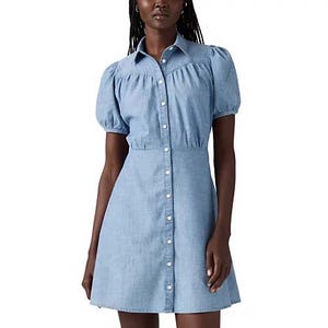 A woman is wearing a light blue, short-sleeved button-down dress with a fitted waist and puff shoulders.