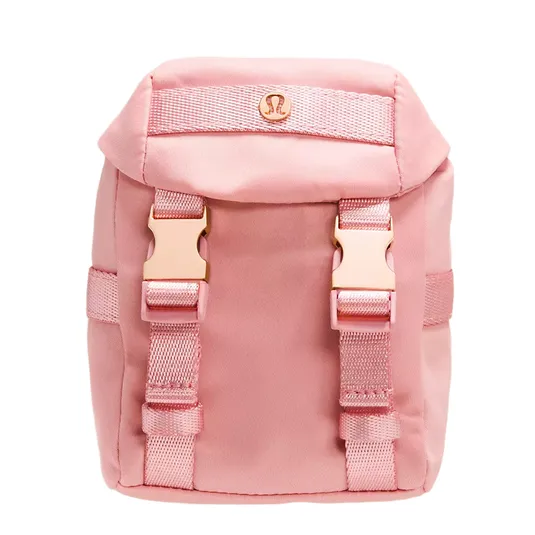 A small pink backpack with two front buckles, featuring a logo emblem on the flap, and adjustable straps, likely designed for casual use.