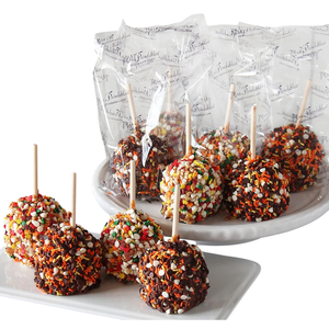 Colorful candy apples coated with chocolate and festive sprinkles are displayed on a platter, with some individually wrapped in clear packaging.