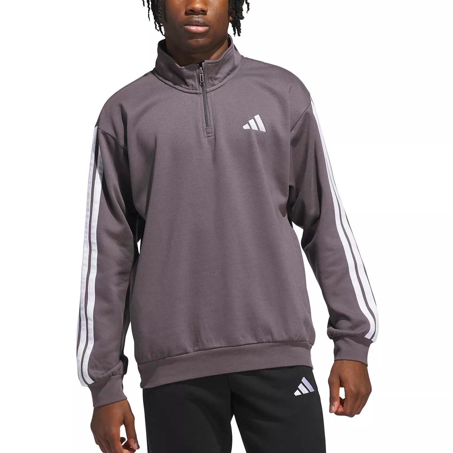 A person is wearing a dark gray Adidas half-zip pullover with white striped sleeves and a logo on the chest, paired with black pants featuring the same logo.