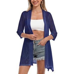 A woman is wearing a sheer blue kimono-style cover-up with 3/4 sleeves, paired with a white tube top and frayed denim shorts.