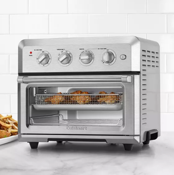 A Cuisinart Air Fryer with a stainless steel finish features an air frying basket inside and four control knobs on the front for cooking settings.