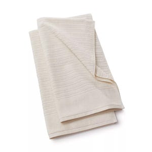 A cream-colored bath towel with a subtle striped texture, folded neatly.