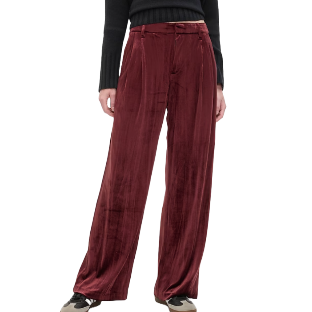 Wide-leg burgundy velvet trousers with front pleats, a high waist, and belt loops, paired with a black long-sleeve top and casual sneakers.