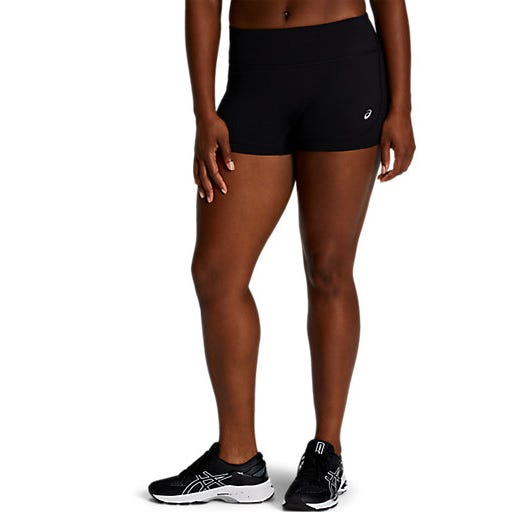 A person wearing black athletic short shorts with a small logo on the side and black running shoes featuring a white sole.