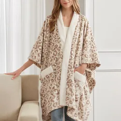 A person wearing a cozy, leopard-print fleece wrap with a white trim and pockets, paired with jeans, near a beige couch.