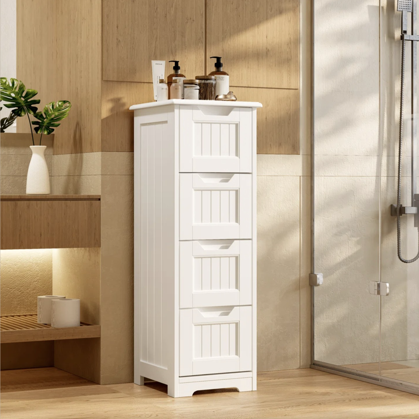 A white, vertical storage cabinet with four drawers, topped with various bathroom essentials like soap dispensers and bottles, stands beside a glass shower.