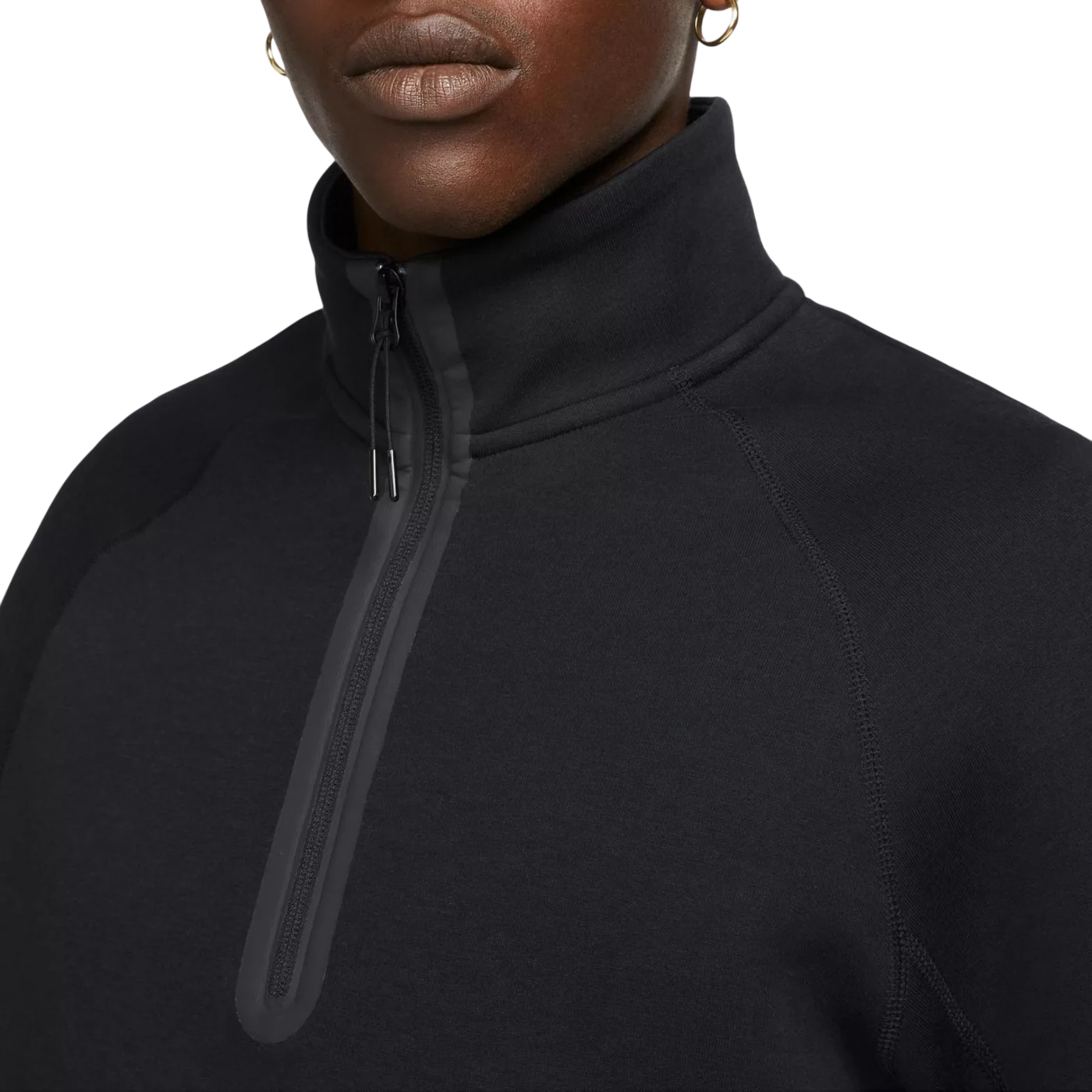 A close-up of a black quarter-zip fleece with a high collar and subtle seam detailing, featuring silver zipper pulls and small gold hoop earrings worn by the model.