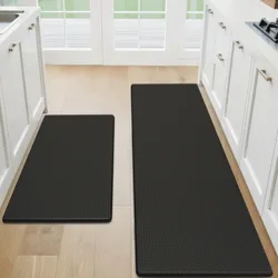 The photo shows two black kitchen mats on a wooden floor in a kitchen, positioned in front of the countertops and a stove area.