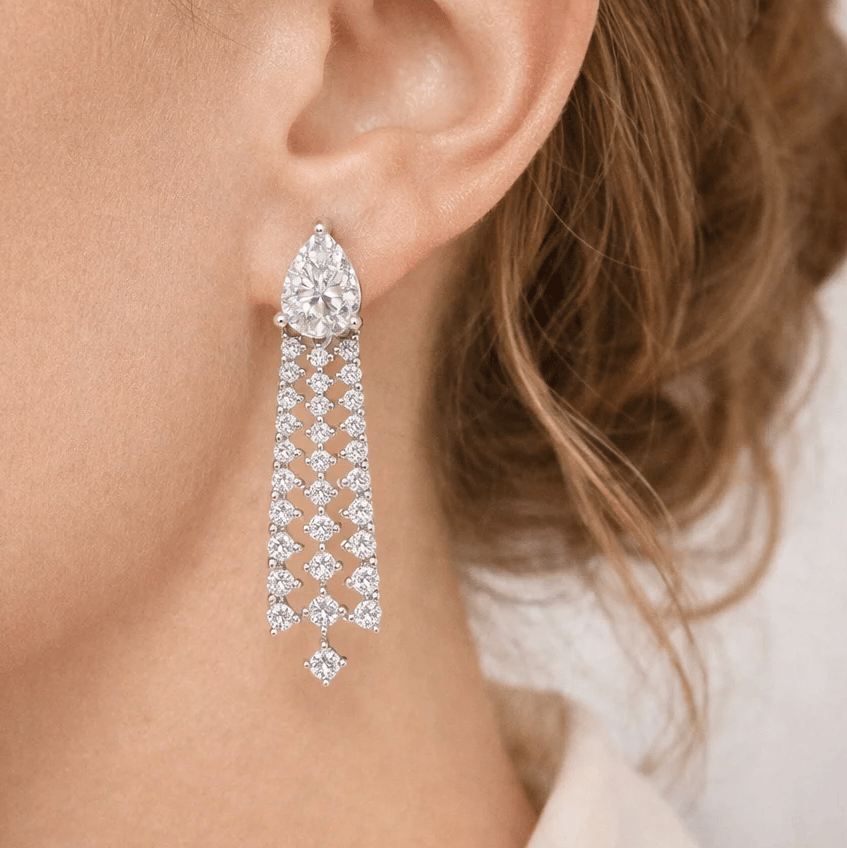 A pear-shaped stud earring features multiple dangling rows of small round diamonds, forming a chandelier design cascading down from the main stone.