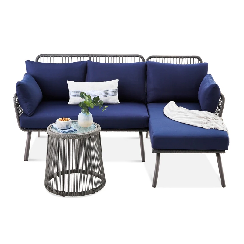 Outdoor sectional sofa with blue cushions, featuring a chaise lounge on the right, accompanied by a small round side table with a glass top, displaying a plant and a bowl.