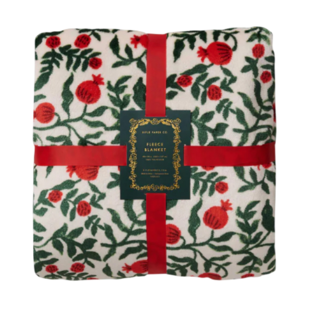 Rifle Paper Co. fleece blanket with a red and green floral pattern featuring pomegranates, wrapped with a red ribbon and a central decorative label.