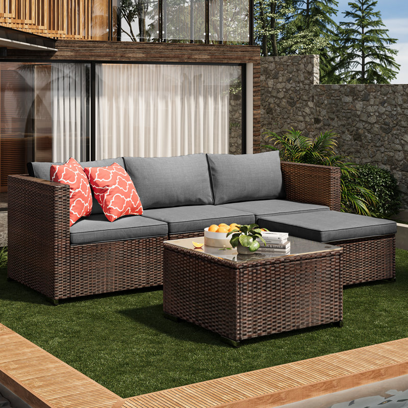 Outdoor wicker sectional sofa with grey cushions and red patterned throw pillows, accompanied by a matching wicker coffee table.