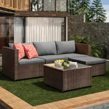 Outdoor wicker sectional sofa with grey cushions and red patterned throw pillows, accompanied by a matching wicker coffee table.