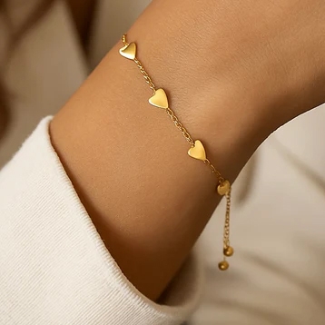 Gold chain bracelet with small heart-shaped charms distributed evenly along the chain. The bracelet is worn on a wrist and features an adjustable clasp with two small dangling beads.