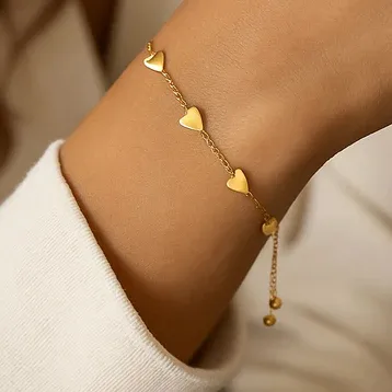 Gold chain bracelet with small heart-shaped charms distributed evenly along the chain. The bracelet is worn on a wrist and features an adjustable clasp with two small dangling beads.