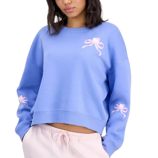 A woman wears a blue sweatshirt featuring pink bows and a small cat graphic on the chest and sleeves, paired with light pink jogger pants.