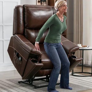 A woman standing next to a brown leather recliner chair with extended footrest.