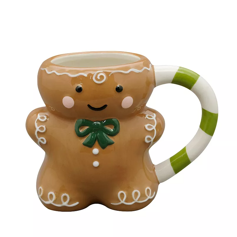 A ceramic mug designed as a smiling gingerbread figure with decorative icing patterns, a green bow on the front, and a handle in green and white stripes.
