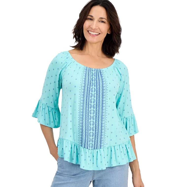A woman is wearing a light blue blouse with three-quarter sleeves and ruffled cuffs, featuring a patterned vertical stripe and ruffled hem, paired with light blue jeans.