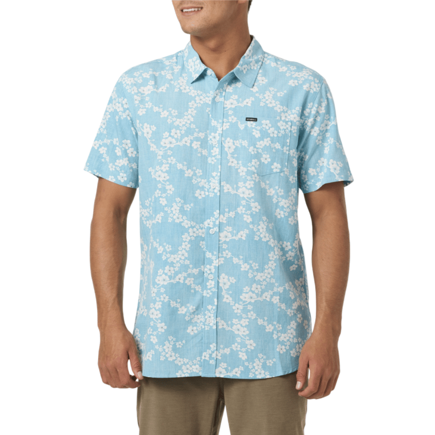 A blue short-sleeve button-up shirt with a white floral pattern and a small logo patch on the chest, worn with khaki pants.