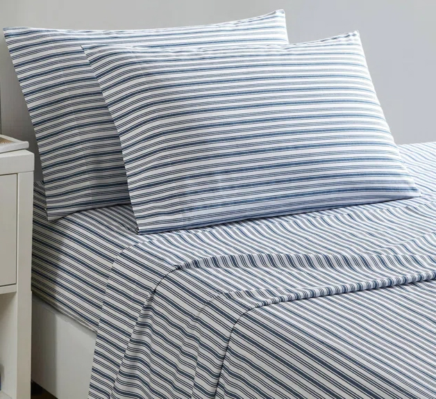 The Nautica Striped Sheet Set features white and light blue horizontal stripes on a bed with matching pillowcases, creating a clean and classic design.