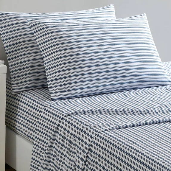 The Nautica Striped Sheet Set features white and light blue horizontal stripes on a bed with matching pillowcases, creating a clean and classic design.