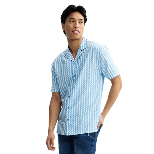 A man wears a light blue and white, short-sleeved, woven camp shirt with a geometric pattern, paired with blue jeans.